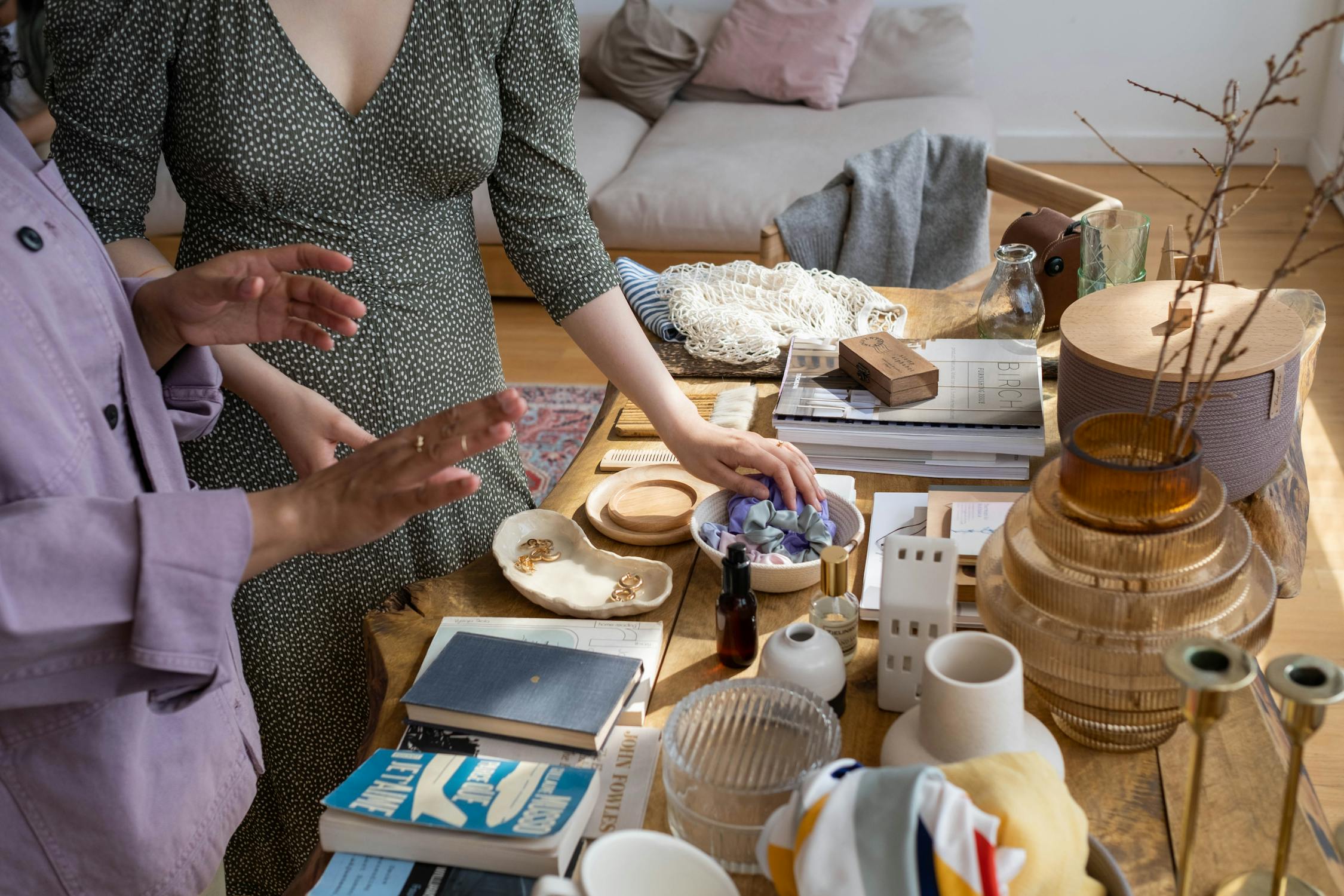 A table with books and objects where two women are having a conversation.